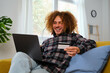 © Ladanifer - Latin young man buying online with a credit card in his laptop at home. Black Friday sales.