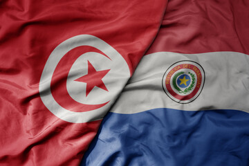 big waving national colorful flag of paraguay and national flag of tunisia .