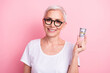 Photo of successful clever woman with short hairstyle wear white t-shirt in glasses holding dollars in hand isolated on pink background