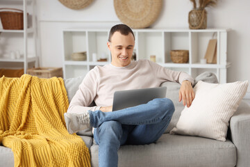 Wall Mural - Young man using laptop on sofa at home