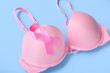© Pixel-Shot - Bra with pink ribbon on blue background, closeup. Breast cancer awareness concept
