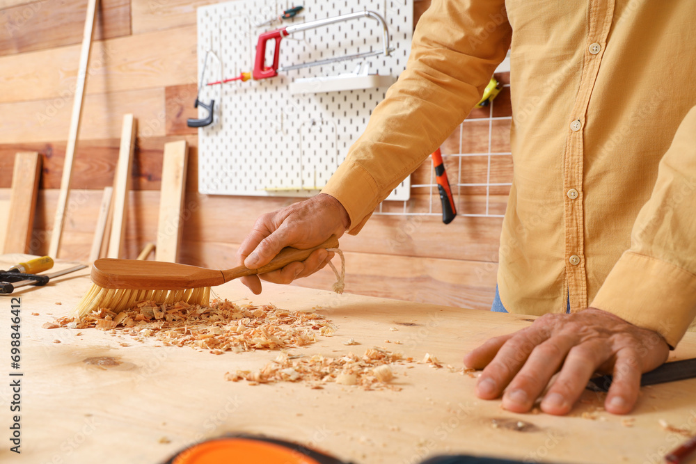Mature carpenter sweeping filings with brush on table in shop, closeup