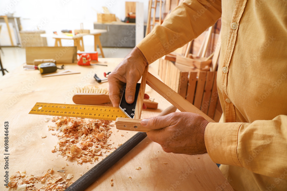 Mature carpenter measuring wooden plank in shop, closeup