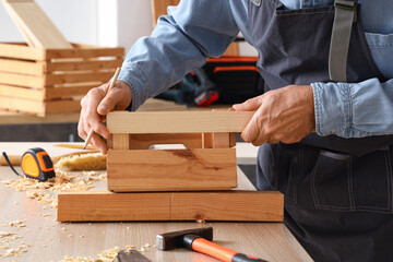 Mature carpenter working with wooden box at table in shop, closeup