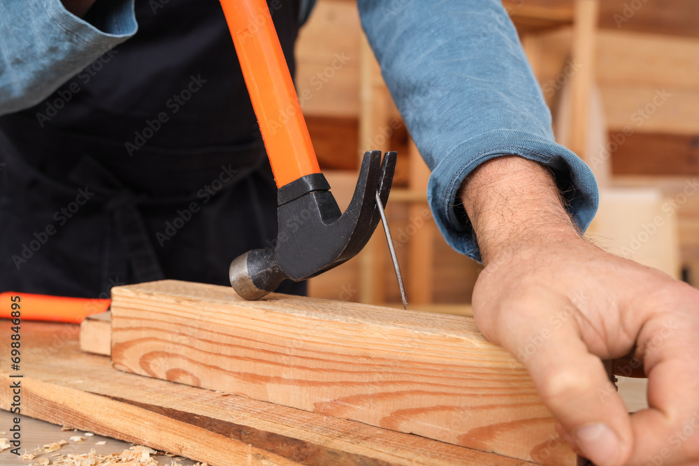 Mature carpenter pulling out nail from wooden plank at table in shop, closeup
