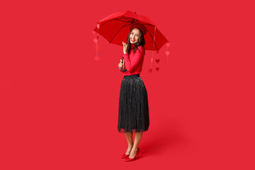 Canvas Print - Beautiful young woman holding umbrella with paper hearts on red background. Valentine's Day celebration