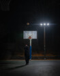 Man throwing a basketball in front of a hoop in front of headlights at night