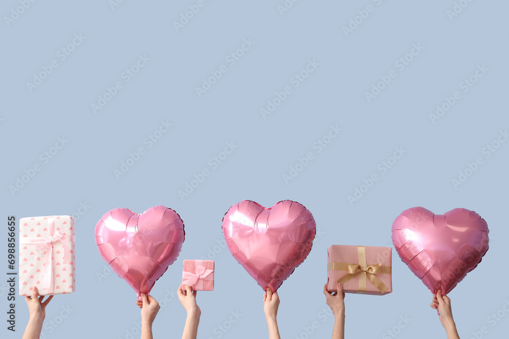 Female hands with gift boxes and heart shaped air balloons on blue background. Valentine's Day celebration