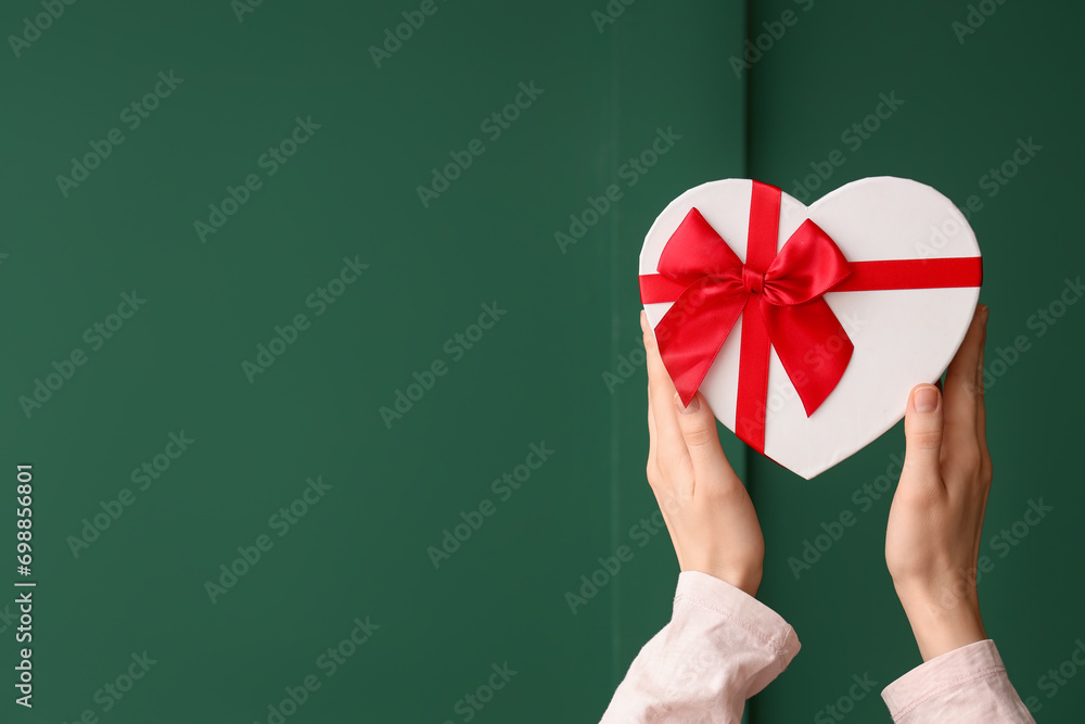 Female hands with gift box on green background. Valentine's Day celebration