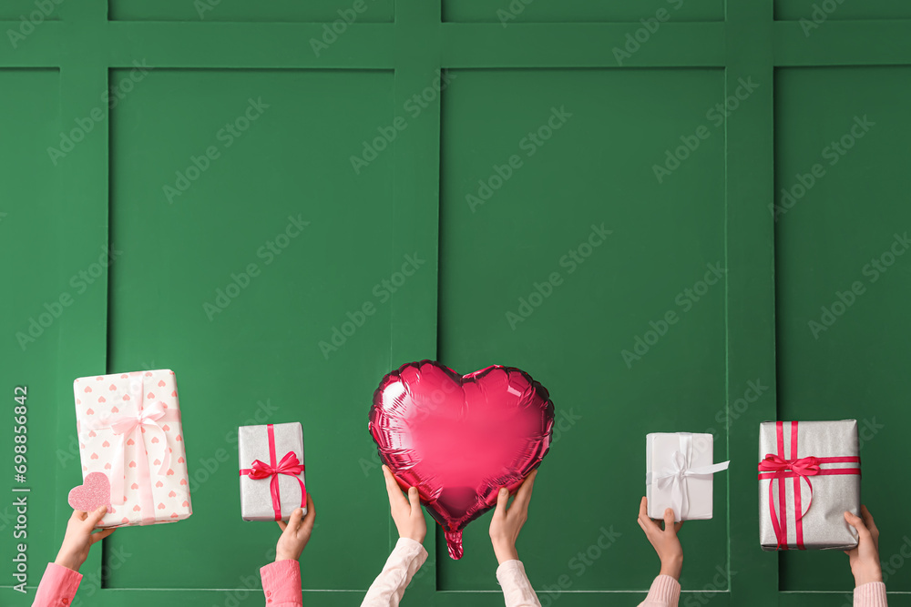 Female hands with gift boxes and heart shaped air balloon on green background. Valentine's Day celebration