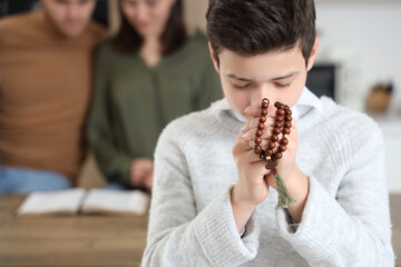 Little boy praying with beads in kitchen, closeup