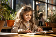 © sofiko14 - Little happy girl in kindergarten reads a book sitting at the table