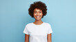beautiful young dark-skinned woman with a lush afro hairstyle in a white t-shirt on a light blue background smiling sweetly