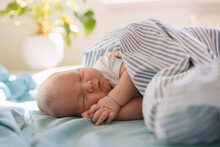 Newborn Baby Boy Sleeping Under Blanket In Bed At Home