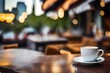 Morning coffe. White cup of coffee on table in outdoors cafe with blurred city street background