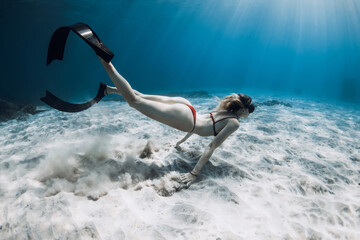 Wall Mural - Woman free diver swims underwater over sandy sea bottom. Freediving in tropical blue ocean