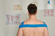 © LIGHTFIELD STUDIOS - back view of man with kinesiological tapes on his shoulders and back during appointment, healthcare