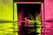 © VISTA by Westend61 - Young man jumping in river water with neon lights under bridge at night