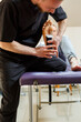 Male physiotherapist doctor massages the feet of a relaxed man sitting on a stretcher. He uses kinesio tape. Taping the foot