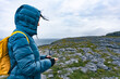 Woman with hood sheltering from the wind on a pristine, natural coastline in Ireland while looking at compass