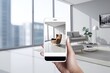 A hand holds a phone with an augmented reality application in a chair in the interior of a modern bright room. AR technology for 3D furniture in the online store.