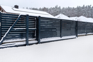 Wall Mural - Modern anthracite panel fence with falling smeared snow during a snowstorm.