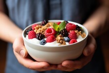 A person holding a bowl of yogurt and berries.