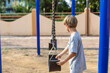 © Татьяна Волкова - Thoughtful preschooler boy, stands near swing, as if deciding whether to try to swing on them.