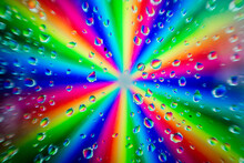 A Radial Burst Of Vibrant Rainbow Colors Blurred Behind A Pattern Of Clear Water Droplets On A Glass Surface