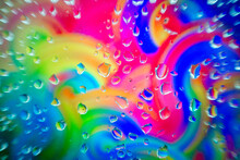 Glass Surface With Water Droplets Over A Swirling, Colorful Abstract Background With Shades Of The Rainbow