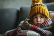 Toddler girl wear hat wrapped in plaid sit alone shivering from cold on sofa