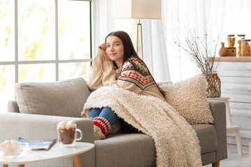 Poster - Young woman with warm plaid sitting on sofa in kitchen