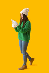 Poster - Young woman in warm hat using tablet computer on yellow background