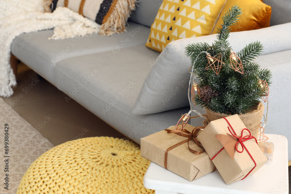 Small Christmas tree with glowing lights, pine cone and gift boxes in living room, closeup