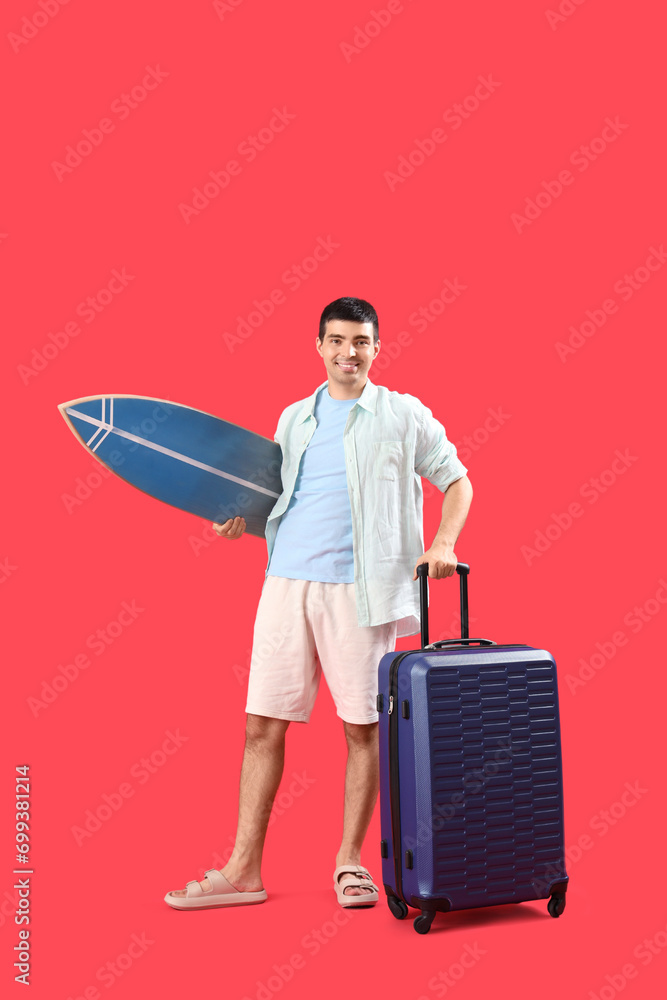 Male tourist with suitcase and surfboard on red background