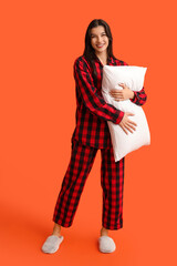 Sticker - Beautiful young woman in checkered pajamas with soft pillow on orange background