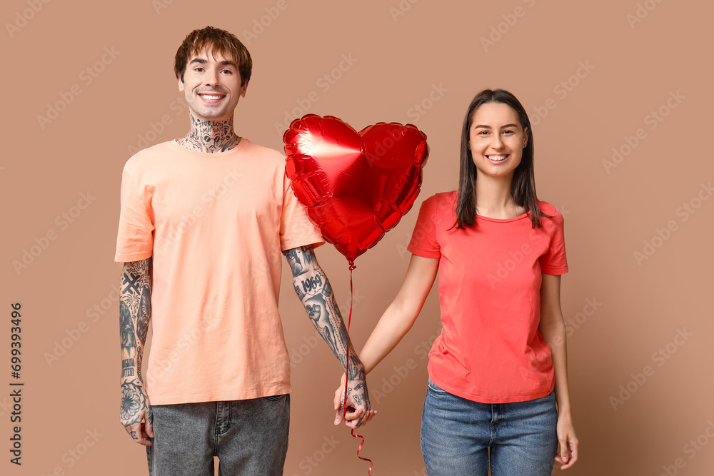 Young couple with heart-shaped air balloon holding hands on beige background