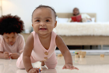 Portrait of smiling African cute toddle baby infant kid crawling on floor with blurred background of curly hair brother boy play toy and father in bed. Happy family spending time together in bedroom.