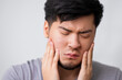 guy with a bad tooth. Asian young guy with a beard stands on a gray background and holds his lower jaw with his hands