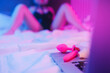 Beautiful woman lies in bed holding clitoral vibrator and watching porn on laptop, neon color. Women has Internet sex chat online