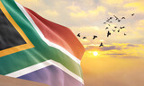 Fototapeta  - Waving flag of South Africa against the background of a sunset or sunrise. South Africa flag for Independence Day. The symbol of the state on wavy fabric.