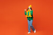 Full body side view young excited cheerful happy woman she wearing green knitted sweater yellow hat scarf do winner gesture isolated on plain orange red background studio portrait. Lifestyle concept.