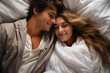 Young couple lying under blanket in bedroom, top view