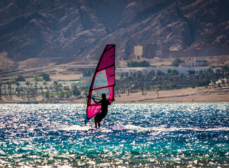 Poster - silhouette of a surfer in the Red Sea on the background of a rocky coast with palm trees and a hotel in Egypt Dahab