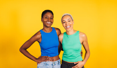 Portrait of a young cheerful female couple in front of a yellow background at studio. Two women together at studio.