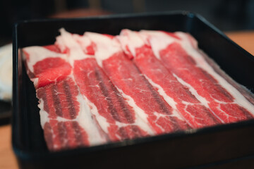 Wall Mural - Thin beef slices for of raw thinly sliced beef served on black tray. Close up