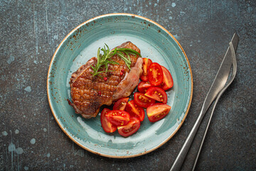 Canvas Print - Delicious roasted duck breast fillet with golden crispy skin, with pepper and rosemary, top view on ceramic blue plate served with cherry tomatoes salad, rustic concrete rustic background