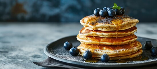 Canvas Print - Sweet pancakes with poppy seeds, yogurt, and blueberries are stacked on a grey stone table for breakfast, with space for copying.