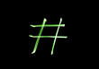 A photograph of a hashtag symbol in vibrant green light in a long exposure photo against a black background. Light painting photography