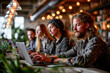 © apratim - A group of young professionals working together on laptops in a modern, stylish coworking space filled with warm lights.